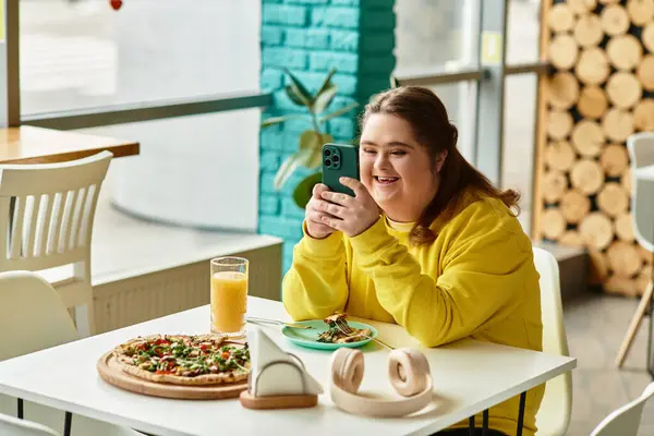 In un vivace bar, una giovane donna sicura di sé con la sindrome di Down si gode il pasto mentre usa il suo telefono. — Stock Photo