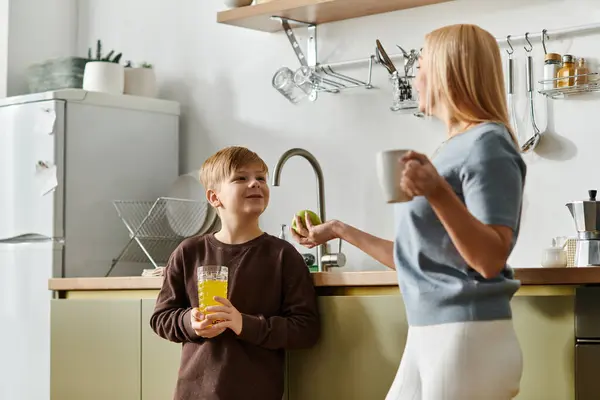A woman engages her son with a smile while they enjoy fresh beverages in a warm kitchen. — Stock Photo