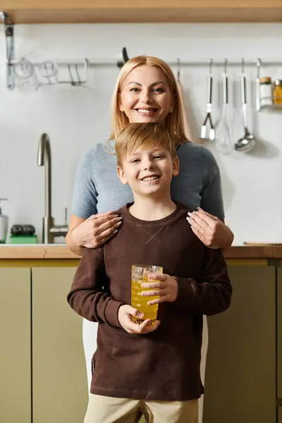 A woman and her son stand together in a modern kitchen, both smiling warmly as they share a drink. — Stock Photo