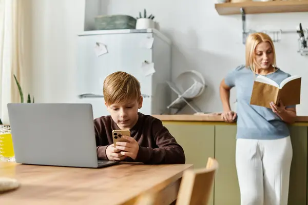 In a cozy kitchen setting, a mother reads a book while her son focuses on his smartphone. — Stock Photo