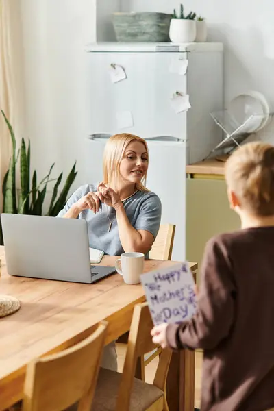Um menino surpreende sua mãe com uma mensagem sentida do Dia das Mães em sua mesa da cozinha. — Fotografia de Stock