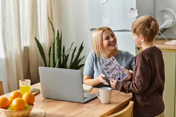 A mother beams with pride as her son surprises her with a heartfelt card, embracing their bond. — Stock Photo
