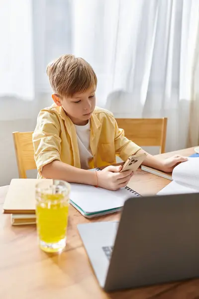 A little boy using his laptop and phone while studying, juice in glass on table. — Stock Photo