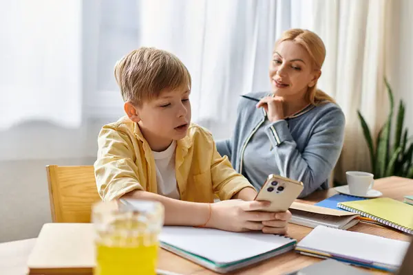 A mother attentively engages with her son as he interacts with a mobile device at a bright table. — Stock Photo