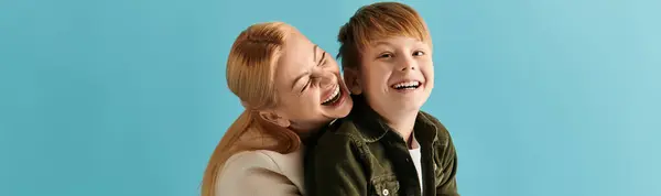 A woman embraces her son with laughter, radiating love and joy in a bright blue setting at home. — Stock Photo