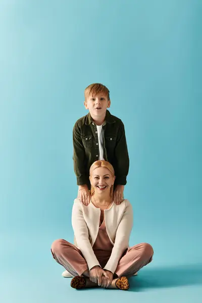 Una madre gioiosa siede sul pavimento mentre suo figlio le sta giocosamente dietro, entrambi raggianti. — Foto stock