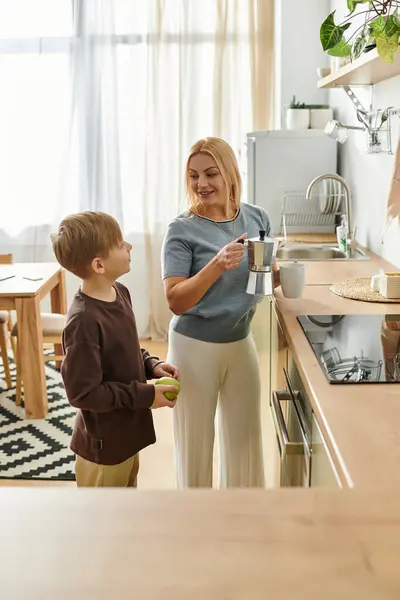 A cheerful mother and son enjoy a fun moment together in their bright kitchen while cooking. — Stock Photo