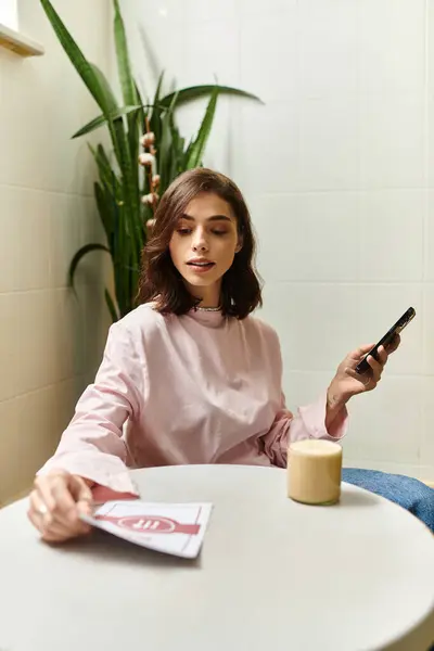 A pretty young woman relaxes in a modern cafe, sipping a drink and checking her phone. — Stock Photo