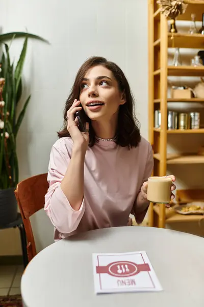A pretty young woman talks on her phone while holding a cup in a modern cafe. — Stock Photo