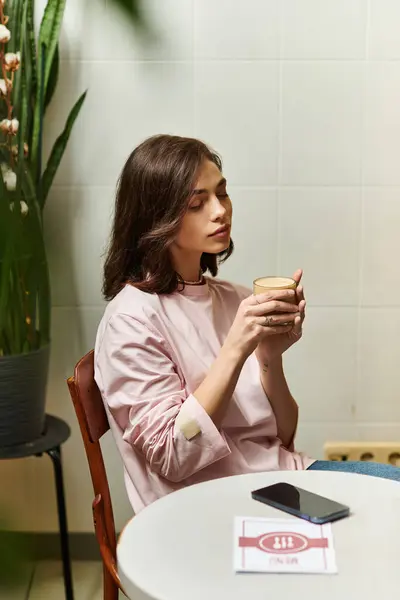 A young woman sips her drink while sitting in a modern cafe, surrounded by greenery and calm vibes. — Stock Photo