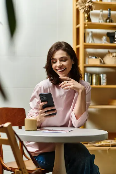 Una bella giovane donna sorride mentre usa il suo telefono, immersa nell'atmosfera accogliente del caffè. — Stock Photo