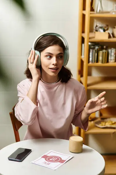 A pretty young woman smiles while wearing headphones, engaged in conversation at a cafe. — Stock Photo