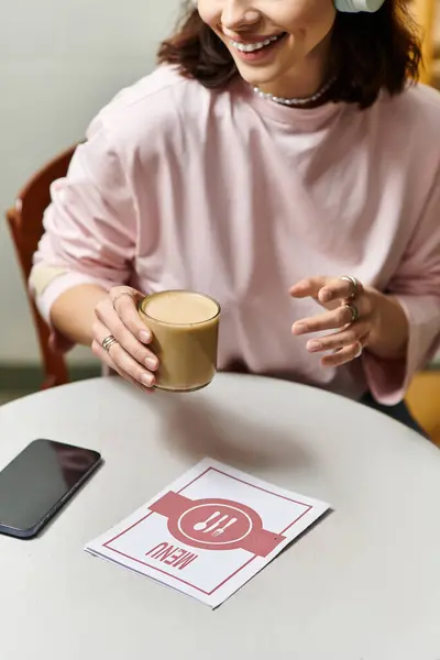 In a cozy modern cafe, a young woman smiles warmly as she holds a drink and examines the menu. — Stock Photo