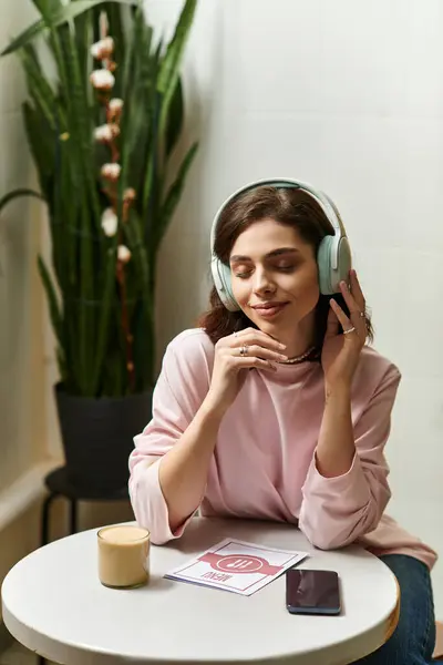 A young woman listens to music with headphones while enjoying a drink in a cozy cafe. — Stock Photo