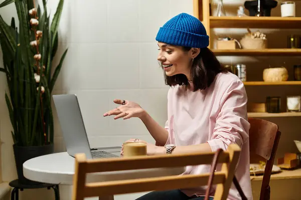 A young woman sits at a modern cafe table, working on her laptop and connecting through video calls. — Stock Photo