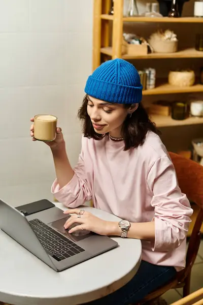Una bella giovane donna che si gode un drink caldo mentre lavora a distanza sul suo computer portatile in un caffè. — Foto stock