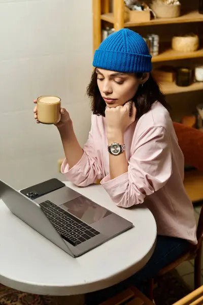 A focused young woman types on her laptop in a modern cafe, savoring a warm drink. — Stock Photo