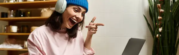 Young woman sports a blue beanie while joyfully working on her laptop in a modern cafe, banner — Stock Photo