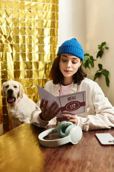 A pretty young woman reads a menu while her labrador sits nearby in a cozy cafe setting. — Stock Photo
