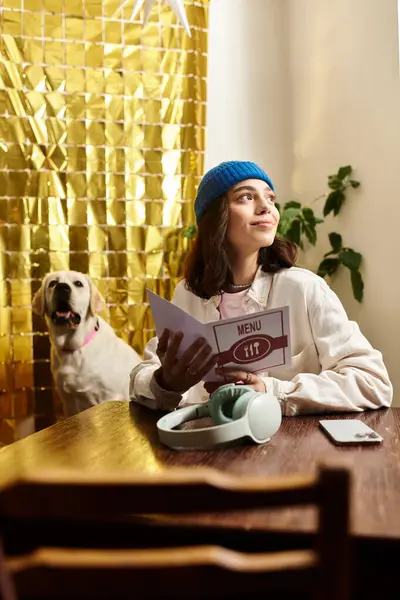 Young woman enjoys her time in a stylish cafe, reading the menu with her labrador by her side. — Stock Photo