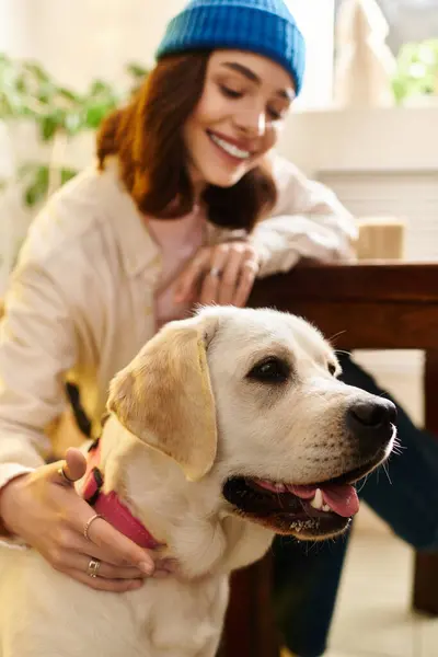 A cheerful woman interacts playfully with her labrador in a contemporary cafe filled with plants. — Stock Photo