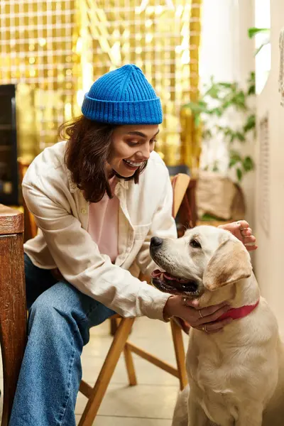 A cheerful young woman interacts lovingly with her labrador in a vibrant cafe setting. — Stock Photo