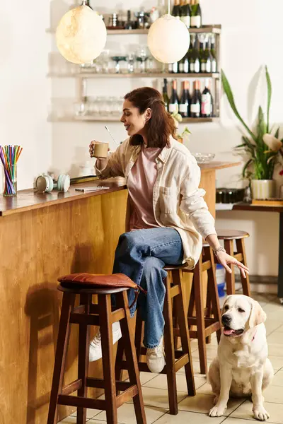 A young woman relaxes in a modern cafe, sipping her drink while her labrador rests beside her. — Stock Photo