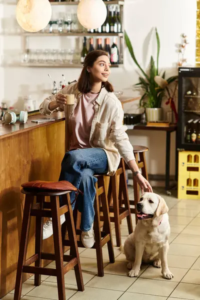 A young woman relaxes with her labrador in a stylish cafe while sipping her warm drink. — Stock Photo