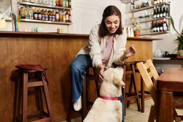A cheerful young woman interacts with her labrador in an inviting cafe atmosphere. — Stock Photo