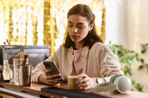 A pretty young woman relaxes in a modern cafe, sipping coffee and focused on her phone. — Stock Photo