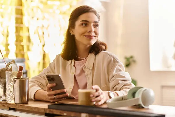 A young woman sits comfortably, sipping coffee and engaging with her smartphone in a modern setting. — Stock Photo