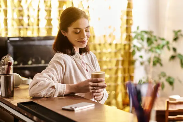 A young woman smiles softly while savoring her drink in a stylish cafe filled with natural light. — Stock Photo