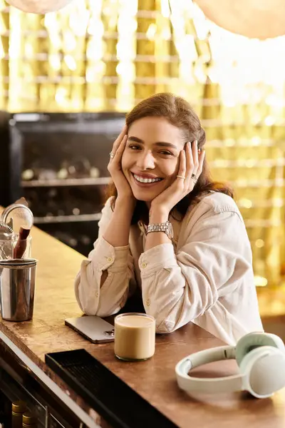 Pretty young woman smiles while resting her head on her hands in a vibrant cafe setting — Stock Photo