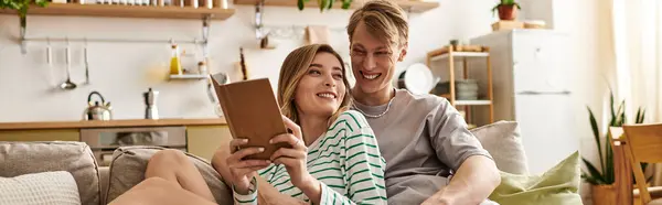 A young couple smiles and relaxes on a couch, sharing a book in their stylish home. — Stock Photo