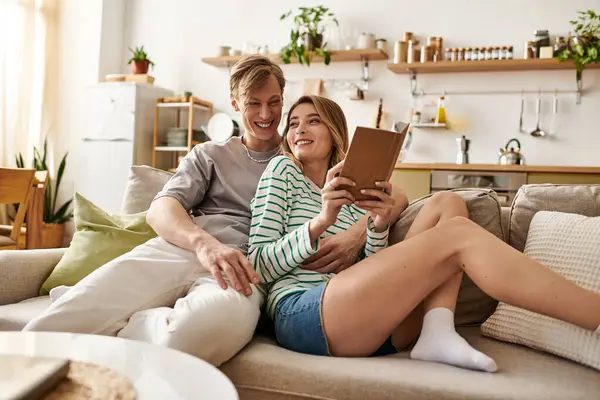 Couple shares laughs and reads together on the sofa in their cozy living room. — Stock Photo