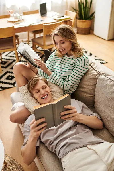 A young couple shares a joyful moment reading together on a cozy couch, surrounded by home decor. — Stock Photo