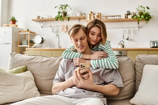 In a cozy space, a young couple cuddles, happily engaging with their phone, surrounded by plants. — Stock Photo