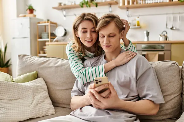A couple laughs together in a warm home, joyfully sharing a moment over a mobile device. — Stock Photo