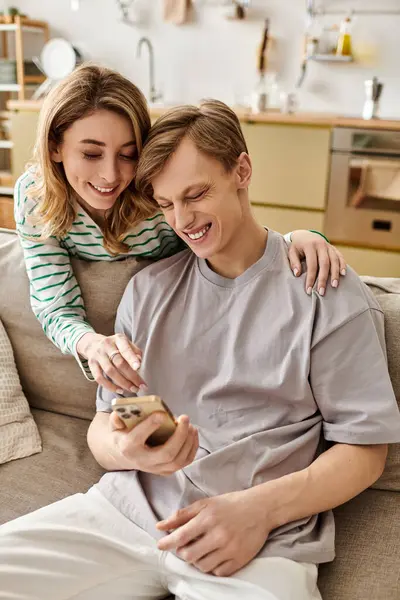 Una giovane coppia a casa condivide risate e gioia mentre usa il proprio smartphone insieme. — Stock Photo