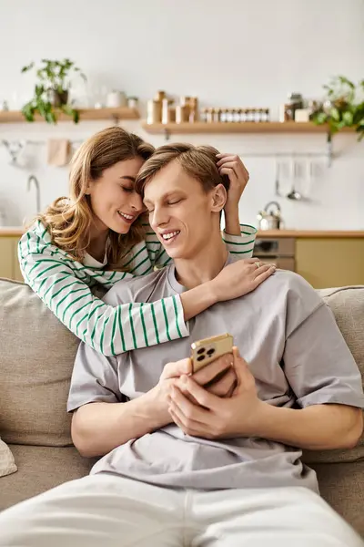 A young couple smiles and embraces on a cozy sofa in their warm, modern living space. — Stock Photo