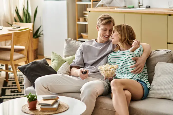 Casal aconchega-se no sofá, compartilhando risos e pipocas em sua elegante sala de estar. — Fotografia de Stock