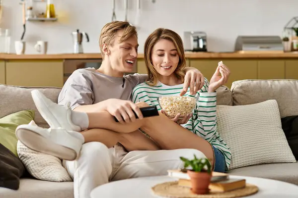 A young couple snuggles on a couch, sharing popcorn and laughter in their stylish home setting. — Stock Photo