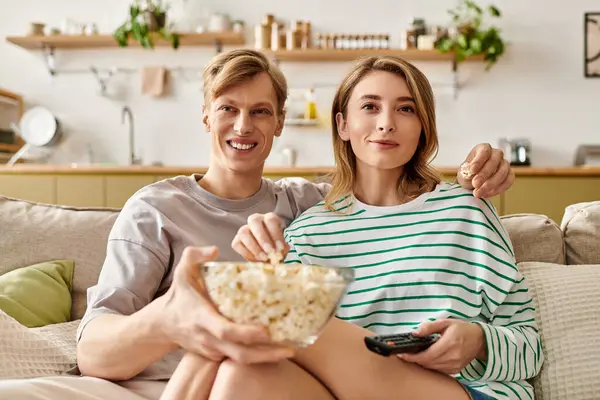 A young couple cuddles on the couch, sharing popcorn and laughter during movie night. — Stock Photo