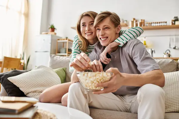 Couple shares a joyful moment at home, savoring popcorn while embracing in a stylish living space. — Stock Photo