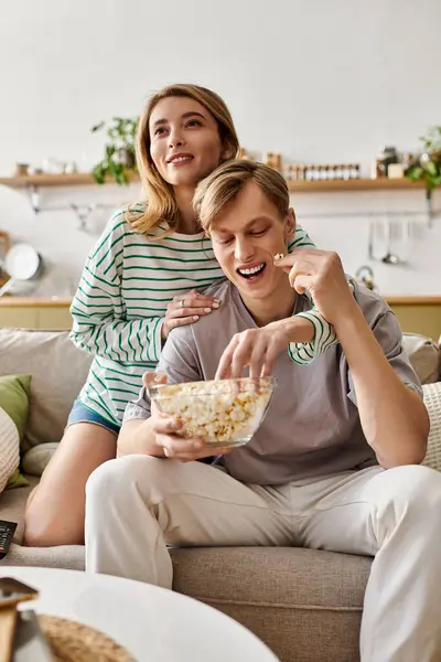 A young couple shares a joyful moment at home, relaxing on the couch with popcorn. — Stock Photo