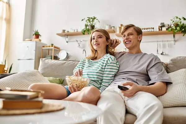 A loving couple relaxes on the sofa, sharing popcorn and laughter while watching a movie at home. — Stock Photo