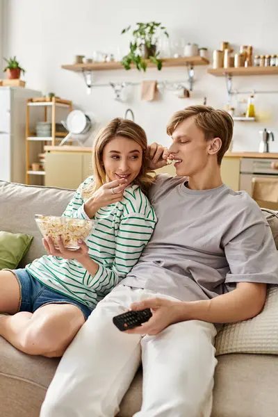 A young couple enjoys a delightful moment at home, sharing popcorn and smiles while relaxing. — Stock Photo