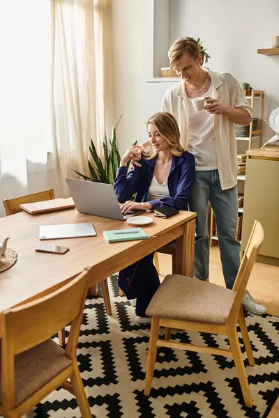 A stylish couple relaxes at home, sharing a light moment while sipping drinks and working together. — Stock Photo
