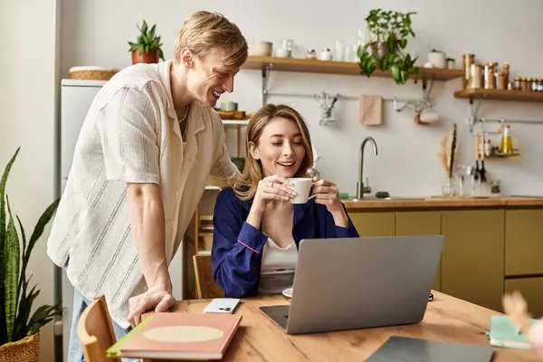 A loving couple shares joyful moments at home, sipping coffee and chatting beside a laptop. — Stock Photo