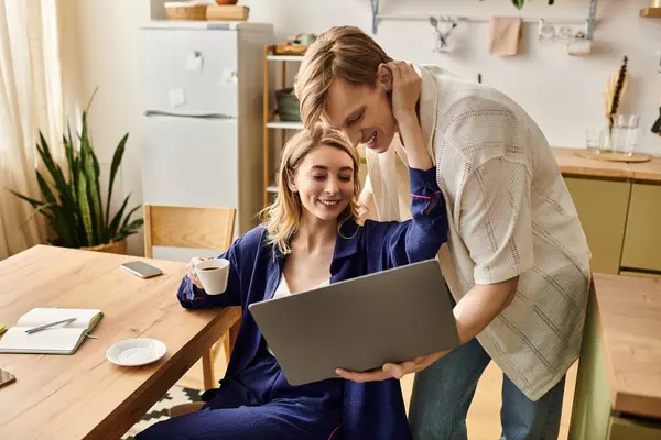 A young couple at home shares a warm embrace over a laptop, sipping coffee and smiling happily. — Stock Photo